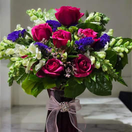 Bouquet of pink roses and purple flowers in a tall vase with a ribbon
