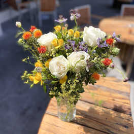 Mixed bouquet of white roses, yellow blooms, and orange flowers in a clear glass vase