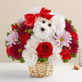 Flower arrangement shaped like a white dog with a red bow and rose in a wicker basket
