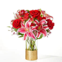Red roses and pink lilies in a clear glass vase with a gold wrap
