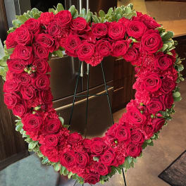 Heart-shaped floral wreath of red roses and carnations on a stand