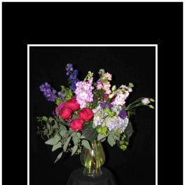 Mixed bouquet of pink, purple, and blue flowers in a clear glass vase