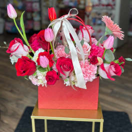 Pink and red flower arrangement in a red gift box with a ribbon handle