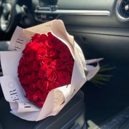 Bouquet of red roses wrapped in white paper on a car seat