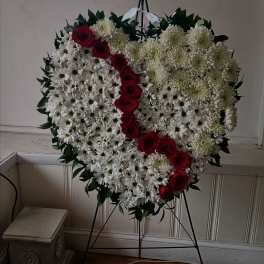 Heart-shaped floral wreath with white daisies and red roses on a stand