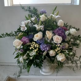 Large white and purple floral arrangement in a white pedestal vase