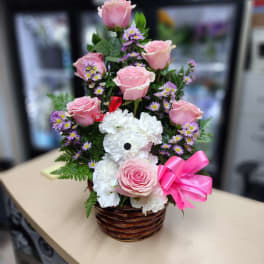 Pink roses and white carnations in a wicker basket with a pink bow