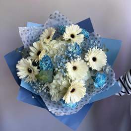 Hand-tied bouquet of white gerbera daisies and blue flowers wrapped in blue and polka dot paper