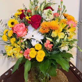 Mixed bouquet of roses, daisies, and yellow blooms in a glass vase
