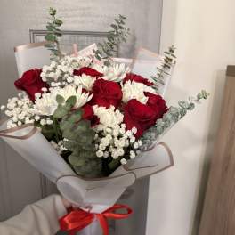 Bouquet of red roses and white daisies wrapped in white paper with a red ribbon