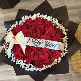 Round bouquet of red roses with a white ribbon and "I Love You" band