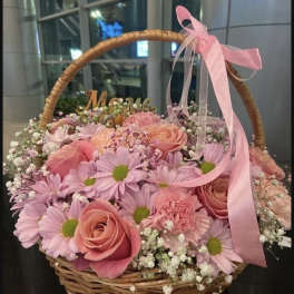 Pink roses and daisies arranged in a wicker basket with a pink ribbon