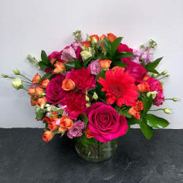 Mixed bouquet of pink, orange, and red flowers in a glass vase