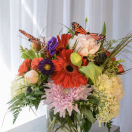 Mixed bouquet in a glass vase with bright flowers and butterfly accents