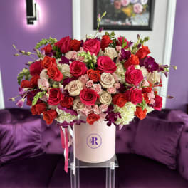 Large hatbox arrangement of red, hot pink, and cream roses with orchids in a blush pink box.