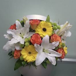 Bouquet of white lilies, yellow gerbera daisies, and orange roses in a white vase