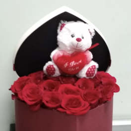 Red roses in a heart-shaped box with a white teddy bear holding a heart