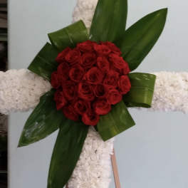 Red rose arrangement on a white floral cross with green leaves