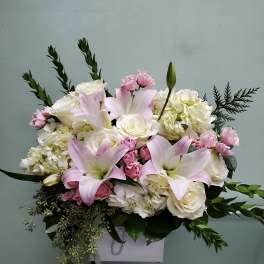 Pink lilies and white roses arranged in a white box with greenery