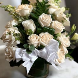 Cream rose bouquet in a glass vase with a white ribbon