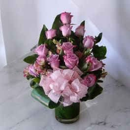Pink roses arranged in a glass vase with a large pink bow