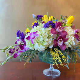 Mixed bouquet in a glass compote vase with purple, yellow, and white blooms