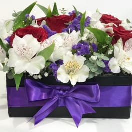 Red and white flowers arranged in a black box with a purple ribbon