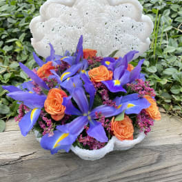 Bouquet of orange roses and purple irises in a white woven basket