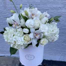 White floral arrangement in a round white box with orchids and roses