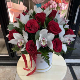 Red roses and white orchids arranged in a white hatbox with a red ribbon