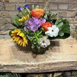 Mixed bouquet with roses, sunflowers, and white daisies in a glass vase