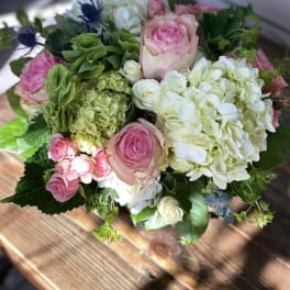 Round arrangement of pink roses with white and green hydrangeas in a low glass vase