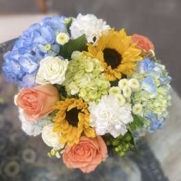 Bouquet of blue hydrangeas, sunflowers, and peach roses