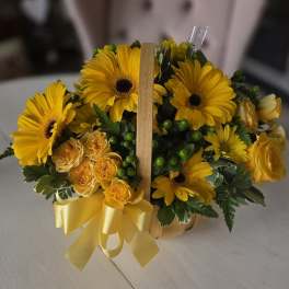 Yellow gerbera daisies and roses in a small basket with a ribbon