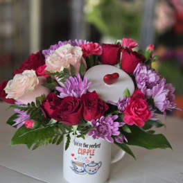 Pink and red flower arrangement in a mug with a heart topper