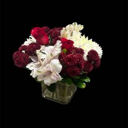 Red roses and white flowers arranged in a square glass vase