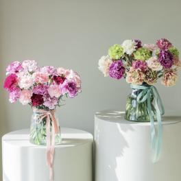 Two bouquets of carnations in glass vases with ribbon ties