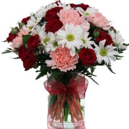Bouquet of red roses, pink carnations, and white daisies in a glass vase