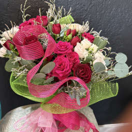 Hand-tied bouquet of red and cream roses wrapped in bright pink and green mesh with ribbon bow