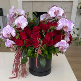 Red roses and pink orchids arranged in a black hatbox