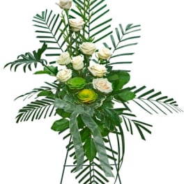 Tall standing spray of white roses with bold palm fronds and a sheer ribbon on an easel