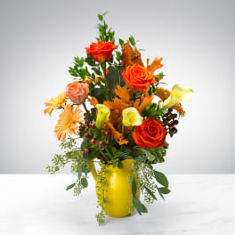 Autumn arrangement of orange roses, yellow calla lilies and peach gerberas in a yellow pitcher vase