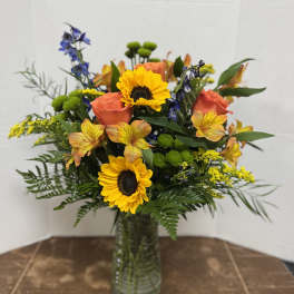 Mixed bouquet with sunflowers, orange roses, and blue flowers in a glass vase