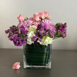 Pink roses and purple flowers arranged in a square glass vase