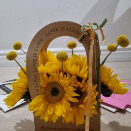 Yellow sunflowers arranged in a cardboard gift bag with a ribbon bow