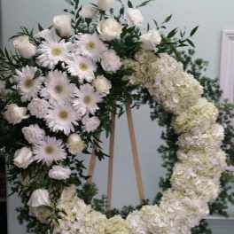 White floral wreath on an easel with roses, daisies, and hydrangeas