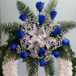 Blue roses and white lilies in a large floral wreath on a stand