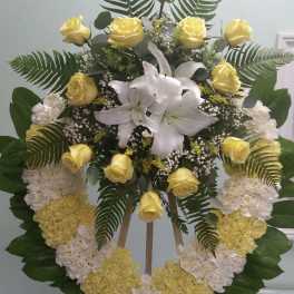 Standing floral wreath with yellow roses, white lilies, and white-yellow carnations