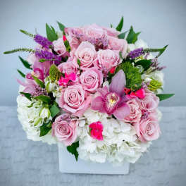 Pink roses and orchids arranged in a white square vase