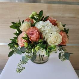 Short round bouquet of peach and cream roses with white hydrangeas in a clear glass vase